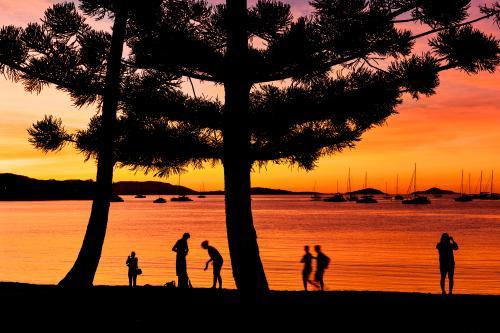 Tropical sunset with sihouettes of people, trees and boats - Australian Stock Image