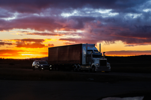 Truck and car driving on highway silhouetted at dusk late in the day - Australian Stock Image