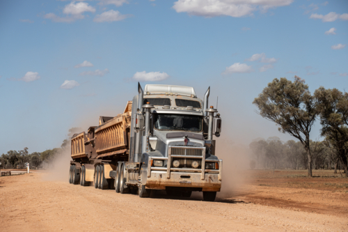 Truck pulling side tippers of gravel along a dirt road - Australian Stock Image