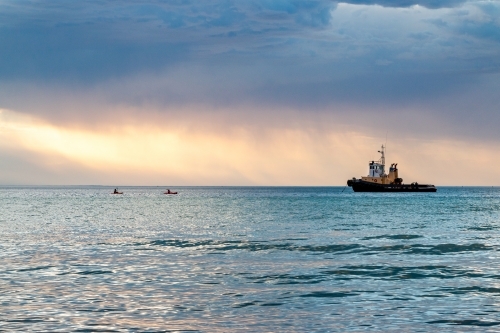 tug boat moored in bay with stormy clouds at sunset - Australian Stock Image