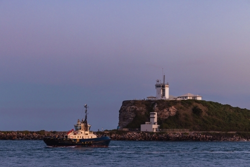 Tugboat passing Nobbys Lighthouse on the headland at the entrance to Newcastle on the Hunter River - Australian Stock Image