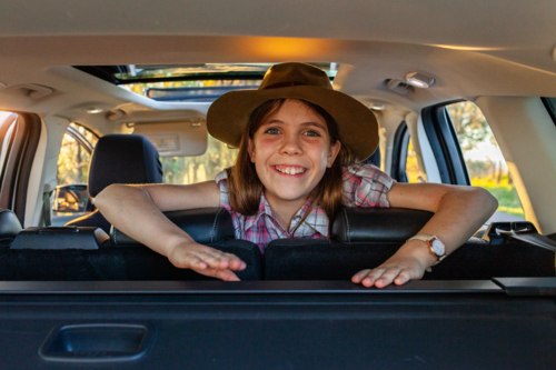 Tween girl smiling looking over back seats of car during road trip - Australian Stock Image