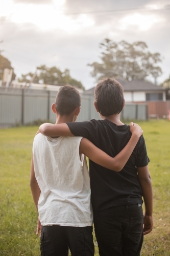 Two aboriginal boys with their arms around one another looking away - Australian Stock Image
