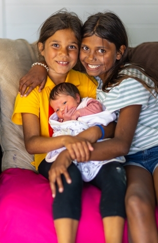 two aboriginal girls sitting on sofa holding a little baby - Australian Stock Image