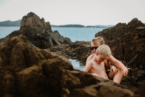 Two boys sitting in a rock pool at Coral Beach in the Whitsundays - Australian Stock Image