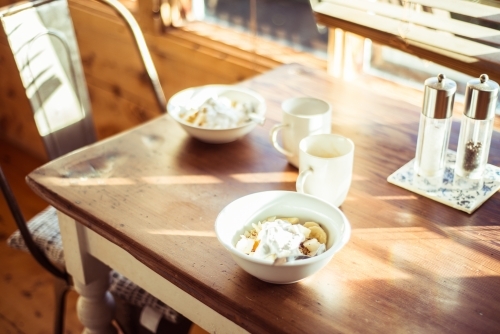 Two breakfast bowls and coffee mugs sitting on a sun drenched table - Australian Stock Image