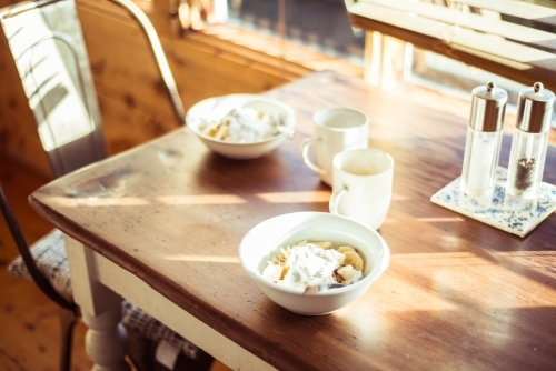 Two breakfast bowls and coffee mugs sitting on a sun drenched table