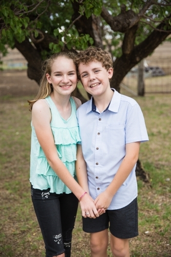Two children cousins standing in yard at home holding hands smiling happy - Australian Stock Image