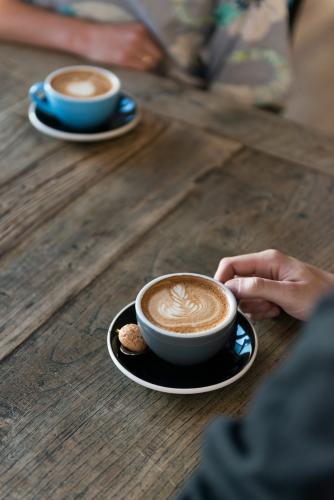 Two cups of coffee on a wooden table with people - Australian Stock Image