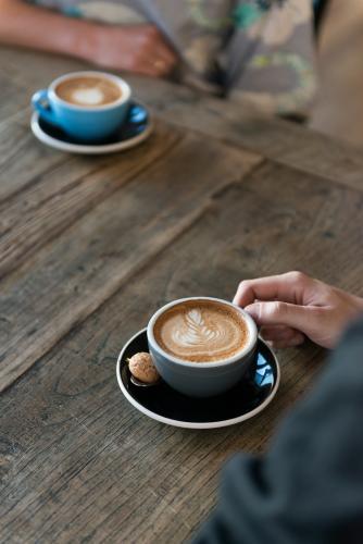 Two cups of coffee on a wooden table with people