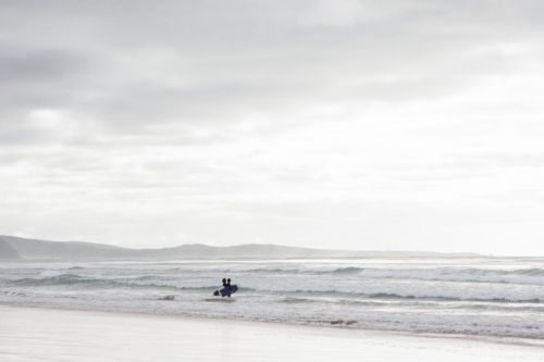 Two distant surfers entering the water - Australian Stock Image