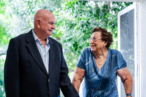 Two elderly individuals engage in conversation while walking through an open door - Australian Stock Image