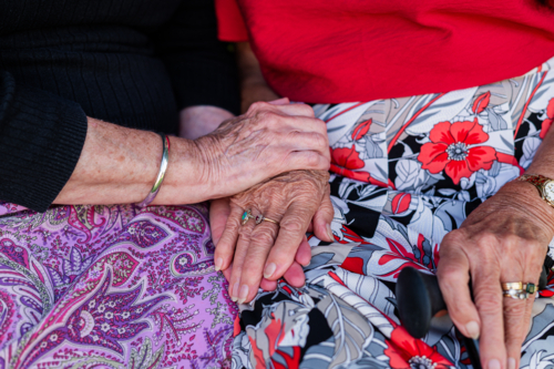 Two elderly individuals sit closely holding hands - Australian Stock Image