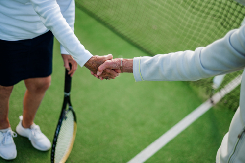 Two elderly women shaking hands, celebrating sportsmanship after their tennis game. - Australian Stock Image