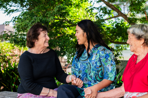 Two elderly women sharing a conversation with female healthcare worker outdoors - Australian Stock Image