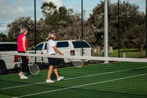 Two elderly women with tennis racquets walking on a tennis court - Australian Stock Image