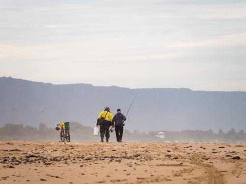 Two fishermen talking on the beach in the distance - Australian Stock Image