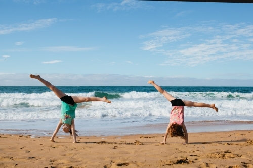 Two girls cartwheeling on a beach - Australian Stock Image