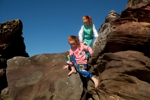 Two girls climbing over rocks - Australian Stock Image