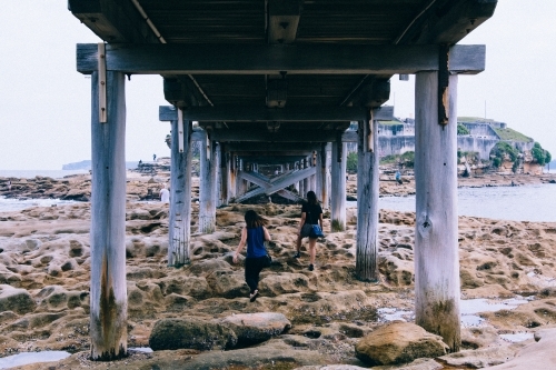 Two girls exploring under a bridge over rocks and water