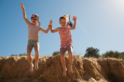 Two girls jumping off a sand dune at the beach