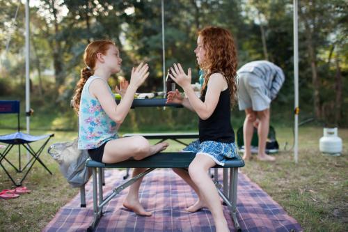 Two girls playing a clapping game at a campsite - Australian Stock Image