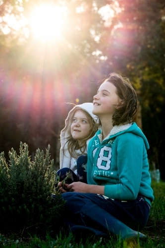 Two girls sitting on grass enjoying the morning sunshine in rural environment - Australian Stock Image