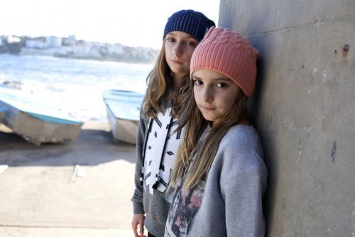 Two girls standing against brick wall posing by the ocean - Australian Stock Image