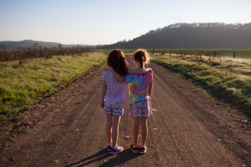 Two girls standing on a dirt road with arms around each other - Australian Stock Image