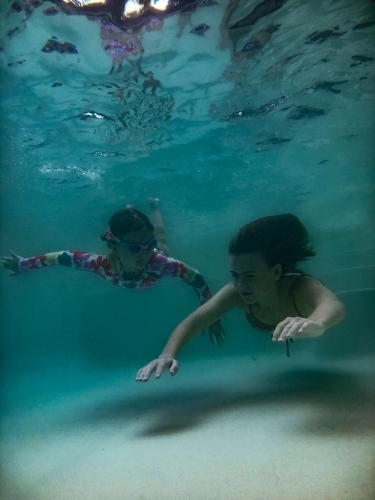 Two girls swimming towards camera underwater in a pool - Australian Stock Image