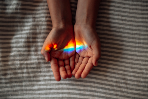 Two hands with palms facing upwards with rainbow-colored light reflection. - Australian Stock Image