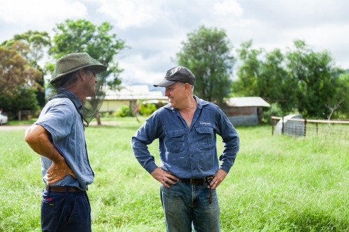 Two happy men talking together in a farm paddock - Australian Stock Image
