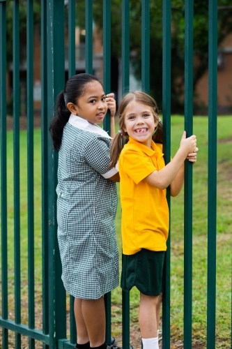 two happy primary school girls swinging off school fence - Australian Stock Image