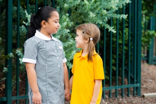 Two happy school friends talking together older girl looking after younger girl - Australian Stock Image