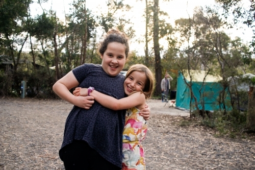 Two happy sister girls hugging each other on holidays at a campground - Australian Stock Image