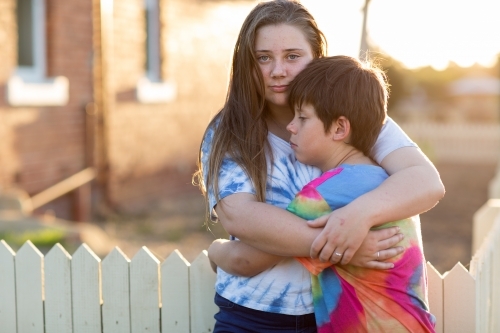 Two kids embracing outside an old house - Australian Stock Image