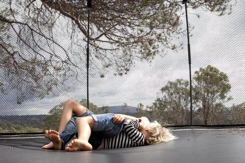 Two kids rolling around wrestling on trampoline in backyard - Australian Stock Image