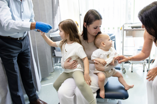 Two kids sitting on mothers lap inside doctors clinic - Australian Stock Image
