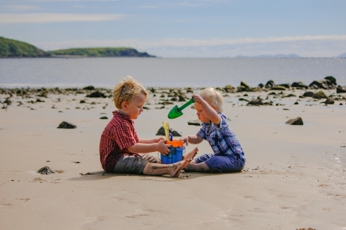 Two little boys playing with buckets and spades on the beach - Australian Stock Image