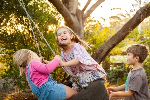 Two little girls on tyre swing in backyard - Australian Stock Image