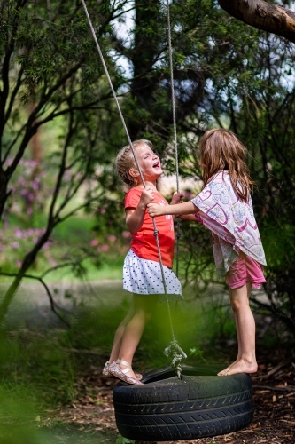 Two little girls playing on a tyre swing on a gum tree in the front yard of a rural property - Australian Stock Image