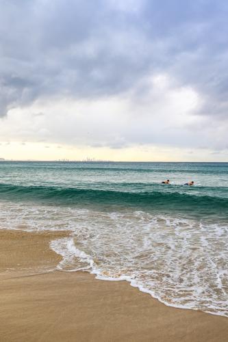 Waves rolling onto a sandy beach at sunrise, with soft morning light reflecting across the water. - Australian Stock Image