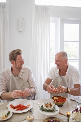 Two men deveining prawns at dinner table