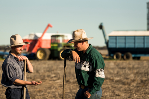 Two men smiling at each other on a field with a blurry tractor behind them - Australian Stock Image