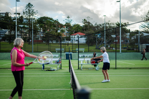 Two older women engage in a friendly tennis match on a overcast afternoon - Australian Stock Image
