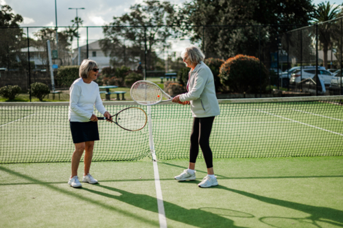 Two older women practice tennis together on a green outdoor tennis court - Australian Stock Image