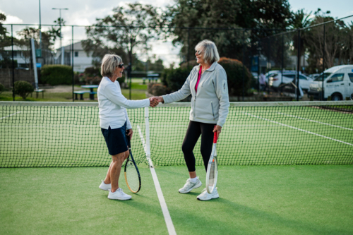Two older women shake hands on a tennis court after a friendly match during daylight - Australian Stock Image