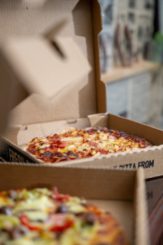 Two open pizza boxes placed on a dark tabletop surface - Australian Stock Image