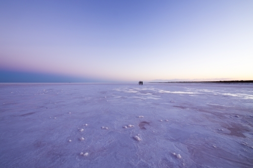 Two people in the distance on a salt lake at dawn