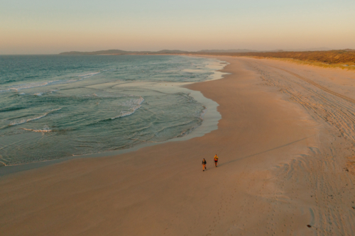 Two people walk along the beach in the soft morning light - Australian Stock Image